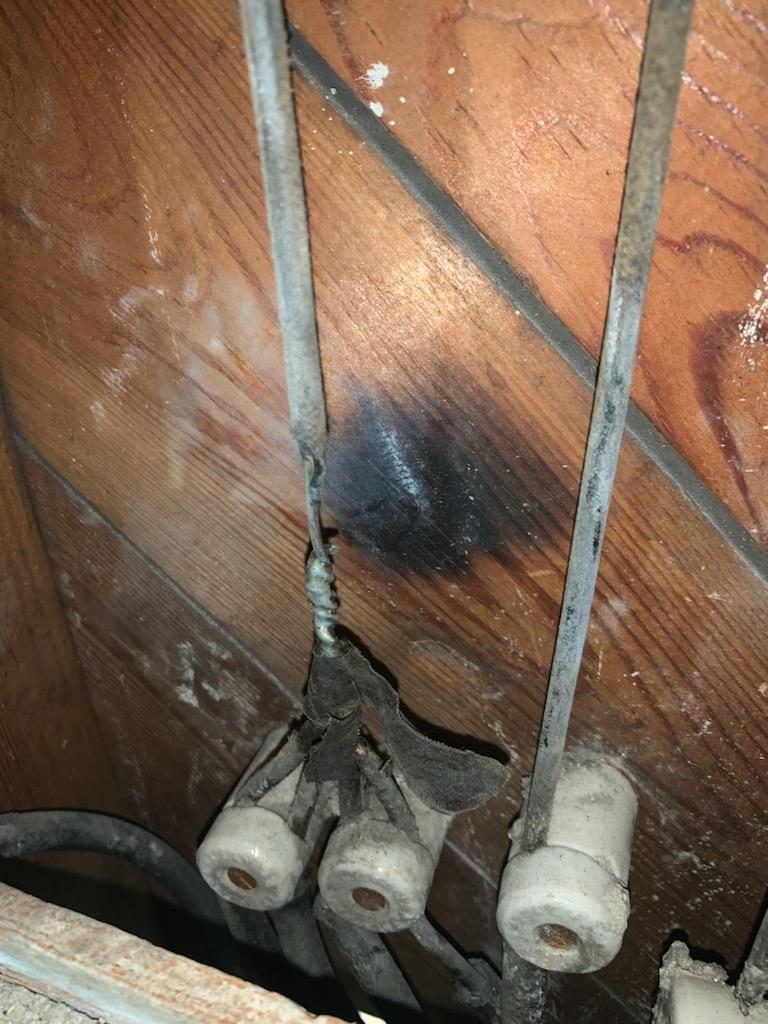 Original knob-and-tube wiring with porcelain knobs and a scorch mark on the wood framing in a 1930s-era Newnan home