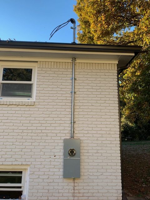 New service mast and meter base installed on the side of a white brick home by Shocking Electric Solutions