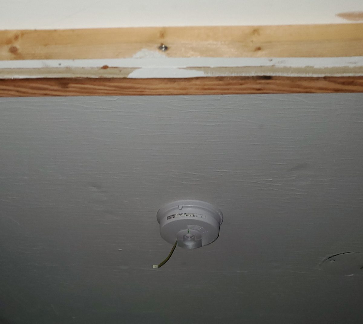 New hardwired smoke detector installed on a ceiling near an exposed wood beam during a renovation